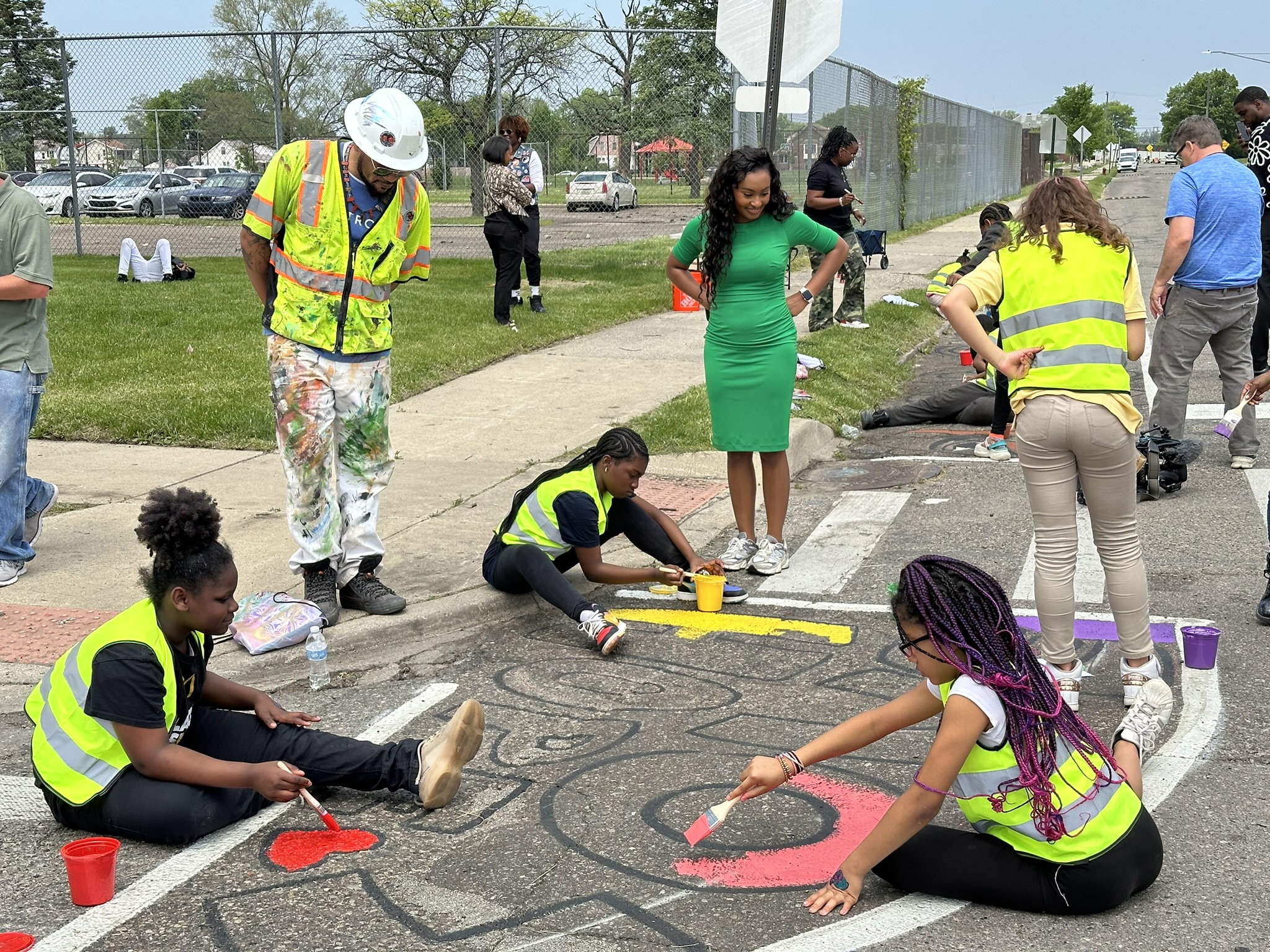 children in safety vests painting words on a street with adult supervision.