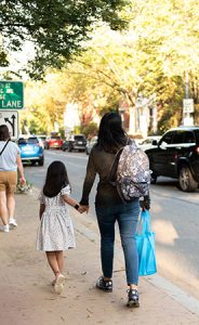 Mother and daughter holding hands walking down a sidewalk
