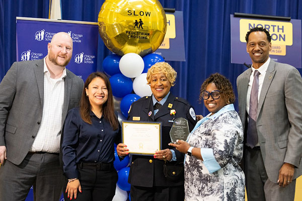four crossing guards receive award from uniformed officer.